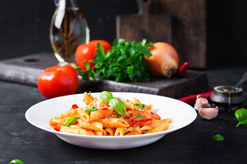 Classic italian pasta penne alla arrabiata with basil and freshly grated parmesan cheese on dark table. Penne pasta with chili sauce arrabbiata.