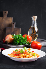 Classic italian pasta penne alla arrabiata with basil and freshly grated parmesan cheese on dark table. Penne pasta with chili sauce arrabbiata.