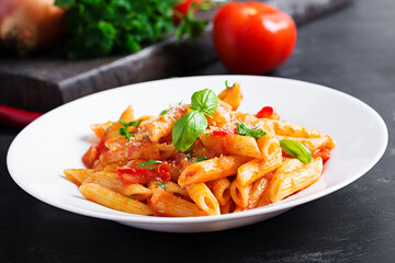 Classic italian pasta penne alla arrabiata with basil and freshly grated parmesan cheese on dark table. Penne pasta with chili sauce arrabbiata.
