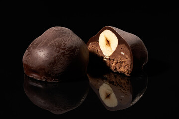 Whole and cut chocolate candy with nut on black background