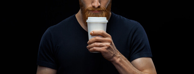 Croped shot of young caucasian bearded stylish man with paper cup of coffee to go over black background. Coffee to go concept.