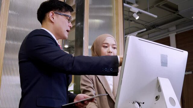 Two male and female hijab business colleagues using digital tablet, computer and discussing project at hotel lobby while standing on desk in hotel lobby prepraing for business. Business concept.