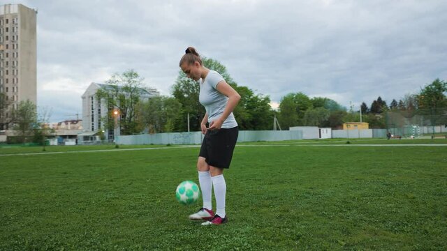 Portrait of woman football player in full growth in the evening park. Woman in professional soccer uniform juggling with ball. Men playing football background.