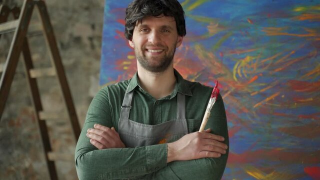 Portrait of a young male artist in his studio. Man artist has his arms crossed and is looking at the camera