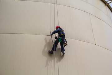 Male worker rope access height safety inspection of thickness storage oil and gas tank