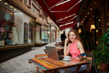 Young girl having tea in a coffee shop. Working with laptop and using a smartphone