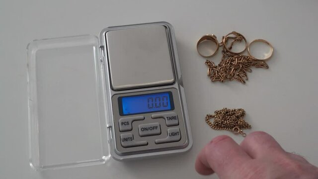 Perspective POV shot of a person measuring the weight of scrap gold jewelry by placing it on a scale.