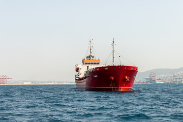 A large cargo ship is in the roadstead in the water area of the Haifa Bay, against the background of Haifa city, in the Mediterranean Sea, near the port of Haifa in Israel