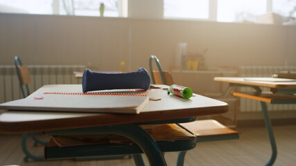 School supplies lying on desk in classroom. Notebook and pencil case on table