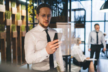 Naklejka na ściany i meble Businessman texting on cellphone in workspace while coworkers having meeting