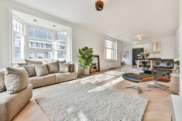 Spacious light living room with large windows and white walls furnished with cozy sofa and armchair...