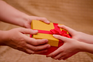 Macro Shot of Mature Woman Hands Holding and Offering Golden Wrapped Gift Box to the Hands of Young Girl.