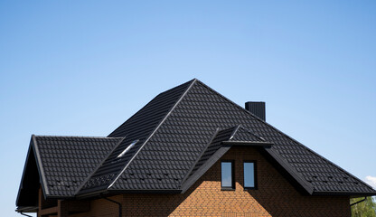 Brown corrugated metal profile roof installed on a modern house with a attic windows. The roof of...