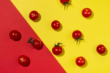 Bright cherry tomatoes whole and sliced in hard light with shadow on geometric red and yellow background, flat lay, food colorful pattern.