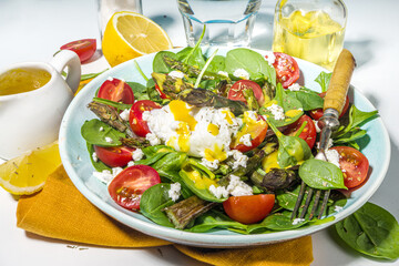 Vegan healthy food, warm asparagus salad with baby spinach, cherry tomatoes, feta cheese and poached egg, light blue sun lighted background top view copy space