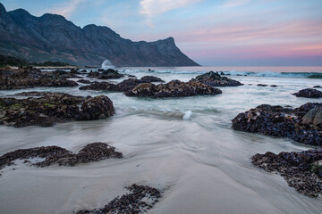 Landscape photo of mountain range ending in the ocean with rocks and ocean in foreground