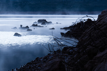 Rocks in a lake or ocean scene sticking out above mist
