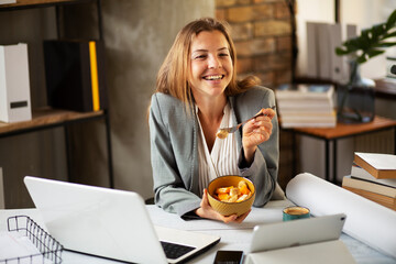 Businesswoman in office having healthy snack. Young woman eating fruit while having a video cal
