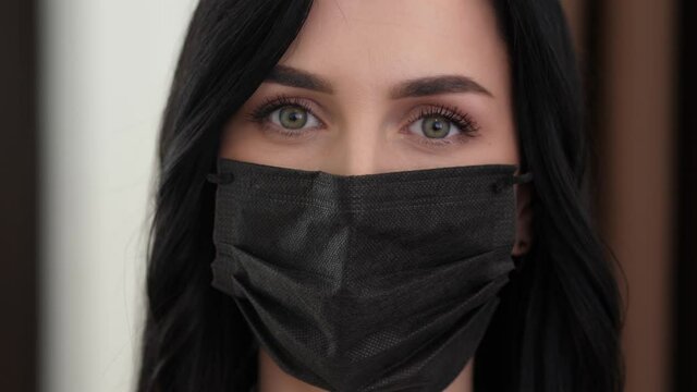 Portrait of beautiful woman putting on face mask against virus bacteria prevention outbreak. Lady brunette wearing protective black mask looking at camera close up