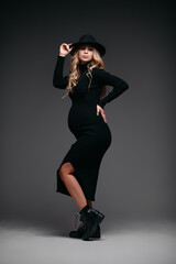 Beautiful pregnant woman in black dress and hat on dark background