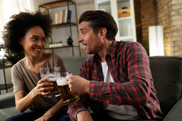 Boyfriend and girlfriend drinking beer at home. Happy couple watching sports game on tv