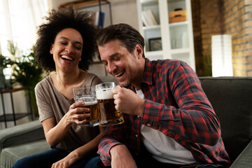 Boyfriend and girlfriend drinking beer at home. Happy couple watching sports game on tv