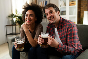 Boyfriend and girlfriend drinking beer at home. Happy couple watching sports game on tv