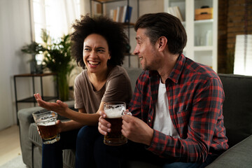 Boyfriend and girlfriend drinking beer at home. Happy couple watching sports game on tv