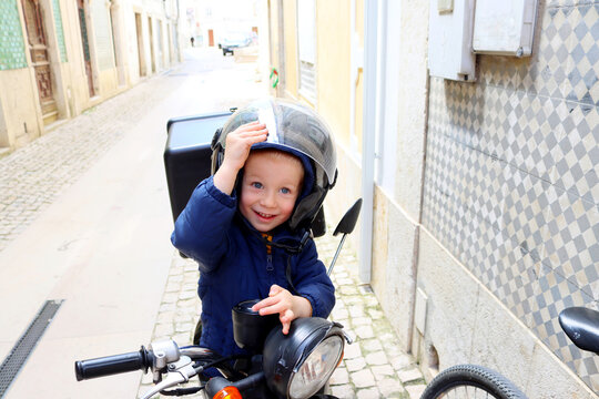 Portrait Of A Happy Little Boy In A Motorcycle Helmet. A Joyful Child Sits On A Motorcycle And Opens The Visor On His Helmet. 