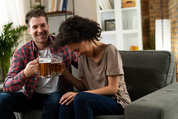 Boyfriend and girlfriend drinking beer at home. Happy couple watching sports game on tv