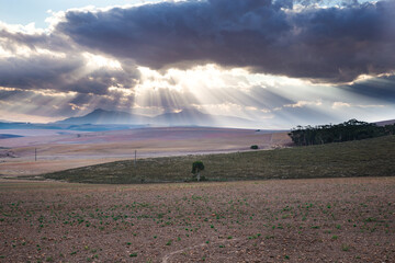 Sunrays burst through clouds over a mountain with farm land in the foreground