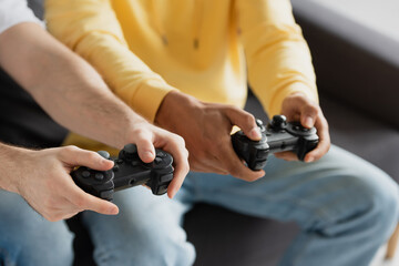 KYIV, UKRAINE - MARCH 22, 2021: partial view of joysticks in hands of interracial men sitting on couch