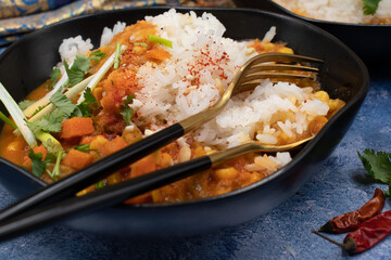 Vegan thai red curry woth rice in stylsih black bowls on textured table