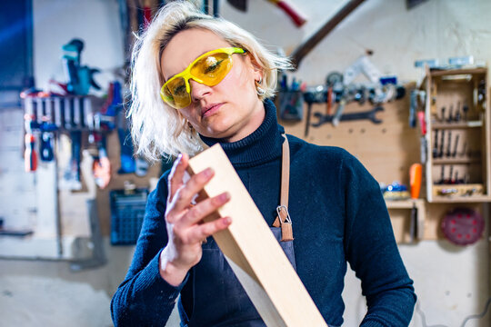 blonde female carpenter using tools for her work in a woodshop
