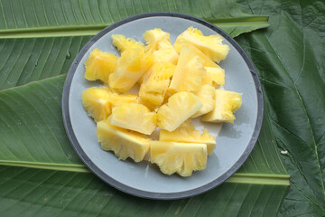 The pineapple is sliced in a plate placed on a green leaf.