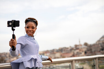 Beautiful african woman taking a selfie in modern city. Cute young woman taking a selfie on a bridge.