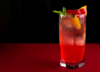 Cold tropical drink, punch with slices of fruits on top, on a black background with ice cubes and a peppermint leaf, glowing and cold summer drink concept