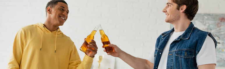 young smiling interracial friends clinking with bottles of beer, banner