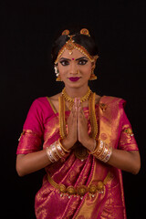 Young South Indian model in bridal red sari with golden jewelry set. Looking at camera. Hands folded in namaste or Indian greeting