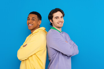 smiling interracial friends in back to back pose isolated on blue