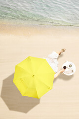 Woman drinking hot coffee with cake sitting at table under beach umbrella near sea coastline of sand beach. Summer vacation. Vertical. Aerial view