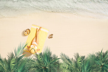 Alone woman in straw hat and bikini sunbathes on yellow beach towel under palm tree branches. Female relaxation on the sand beach at summer vacation. Top view