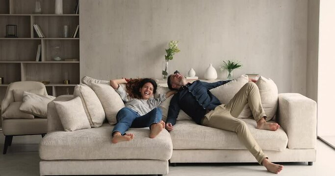 Happy Hispanic couple jumping on soft sofa laugh enjoy relax, rest on cozy couch feel overjoyed celebrate move day to own home, rented flat. Homeowners family, fashionable furniture store ad concept