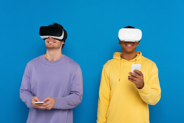 interracial hipsters in virtual reality headsets and smartphones isolated on blue