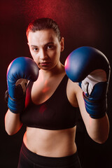 Strong sport woman boxer wearing blue boxing gloves on dark red background