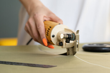 Electric tool for cutting textile. Closeup of female hand hold cutter while working with fabric for...
