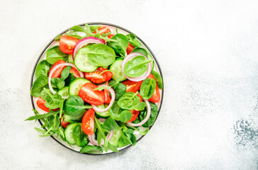 Summer vegan salad with spinach, tomatoes, arugula, cucumber and red onion. Fresh and Healthy food. Gray stone table. Top view