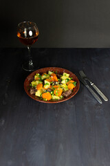 plate with stew cooked of vegetables and beef, rose wine glass, cutlery on black background