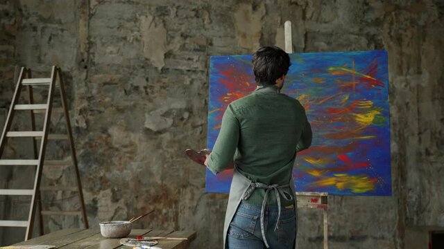 Male artist approaches the painting and makes strokes with a brush