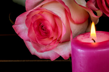 Fototapeta premium A candle is burning next to white-red roses